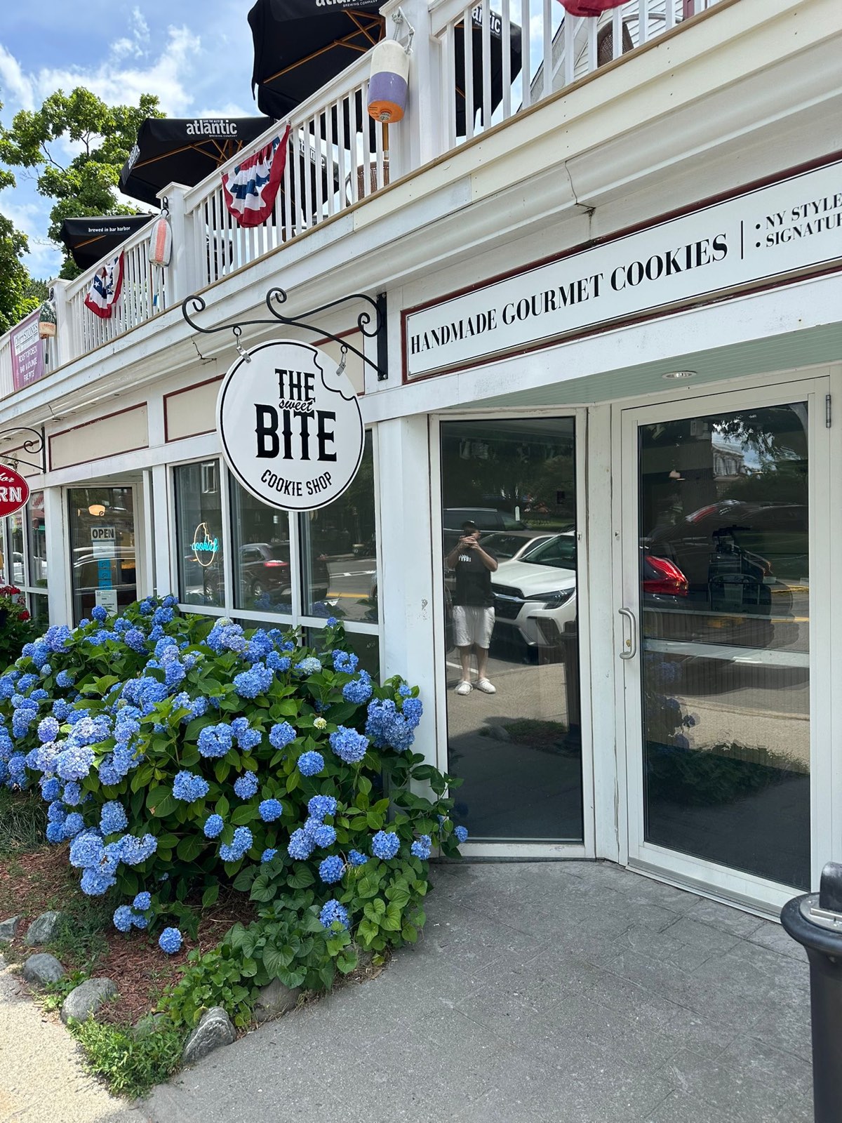 The shop's round hanging sign above a bank of blue hydrangeas by the front door.